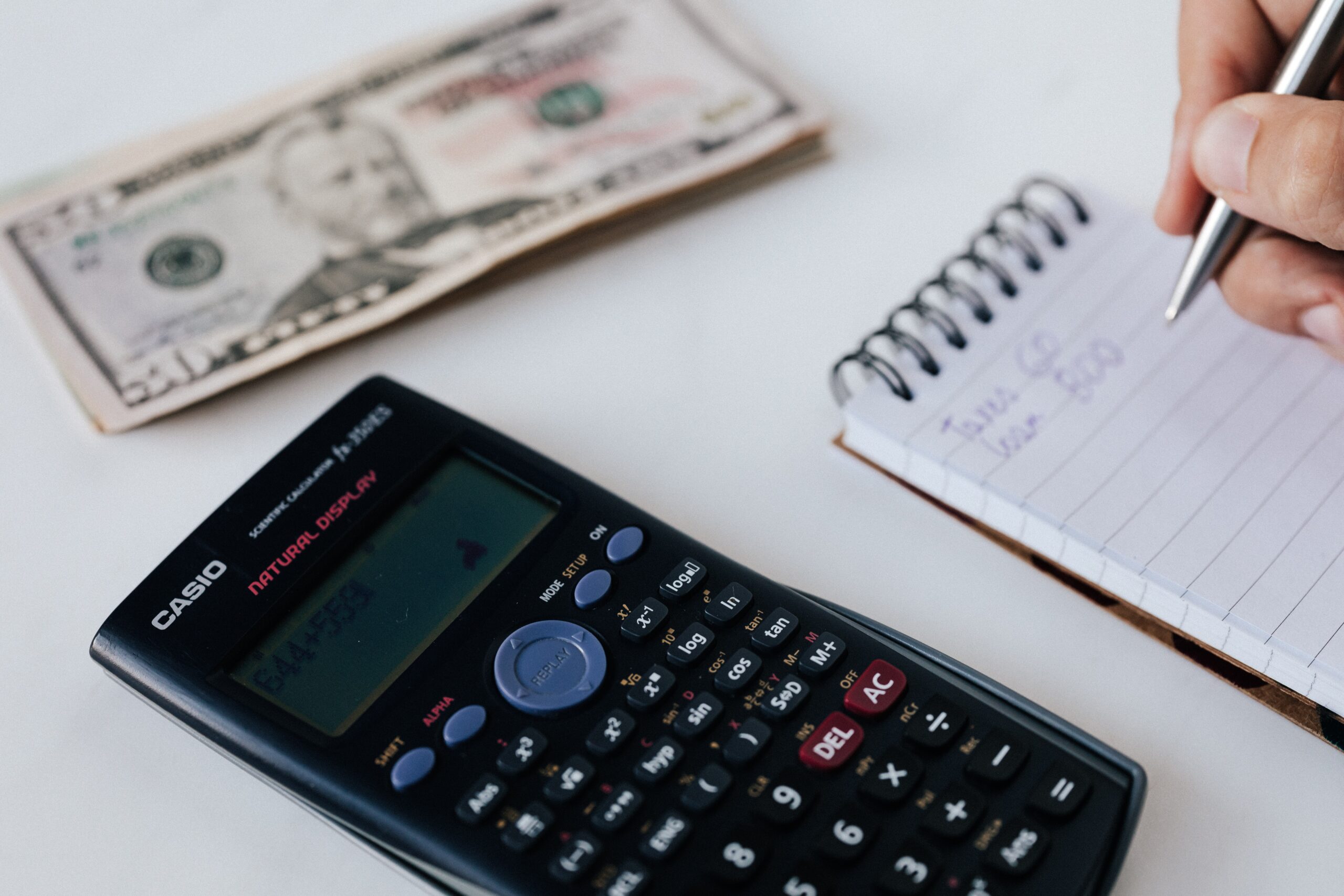 A notepad, a calculator, and dollar bills on a desk
