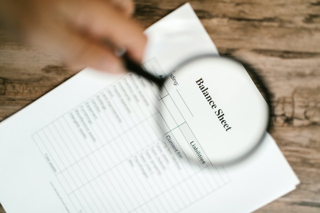 A person holding a magnifying glass over a balance sheet.