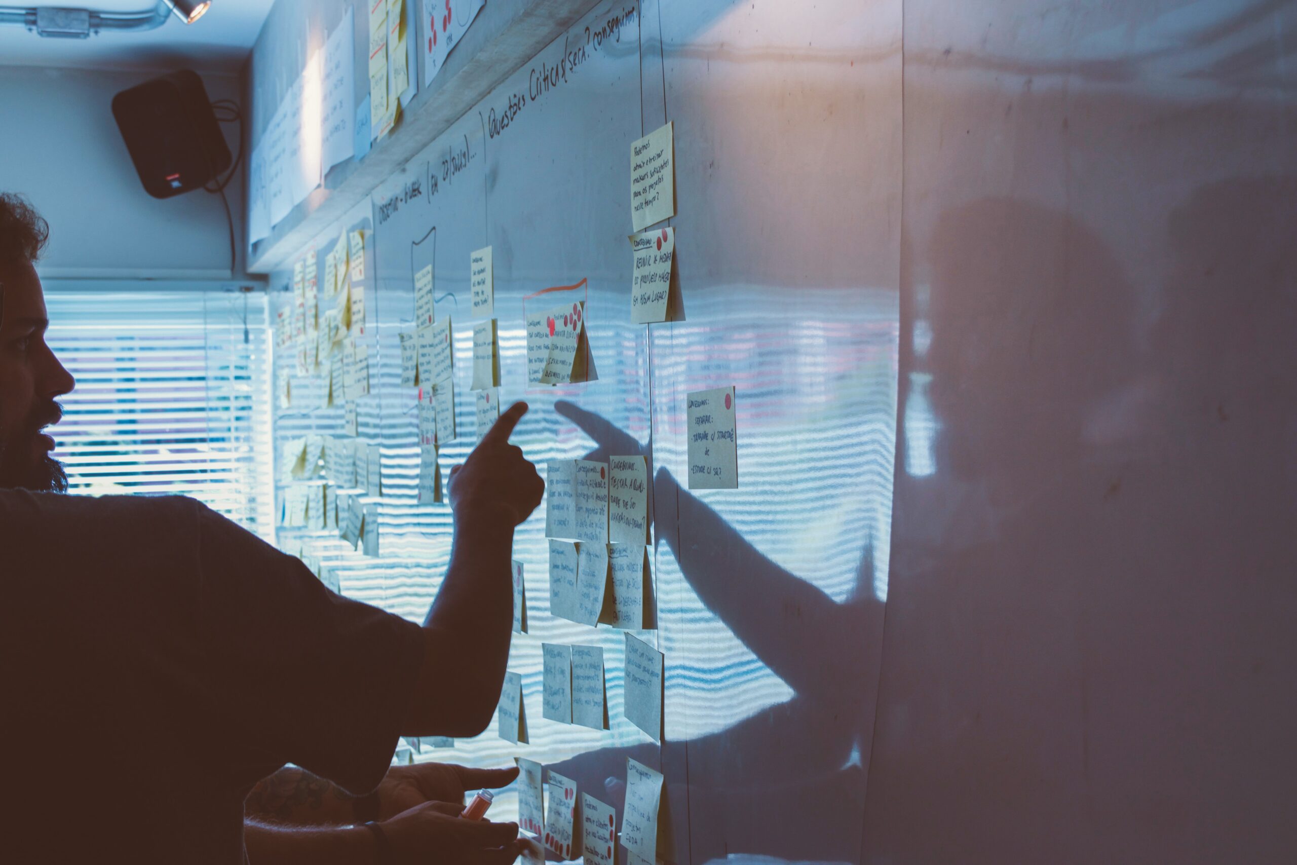 A man points to a whiteboard with notes stuck on it.